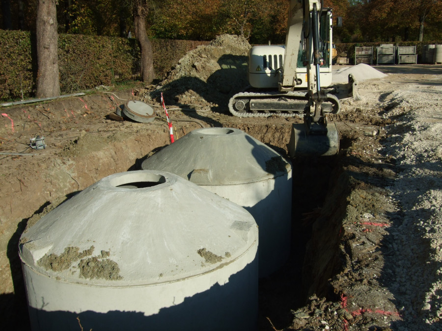 Große Wasserbehälter sind in einem offenen Graben versenkt am Kompostplatz des Hofgartens Ansbach, in Hintergrund steht ein kleiner Bagger